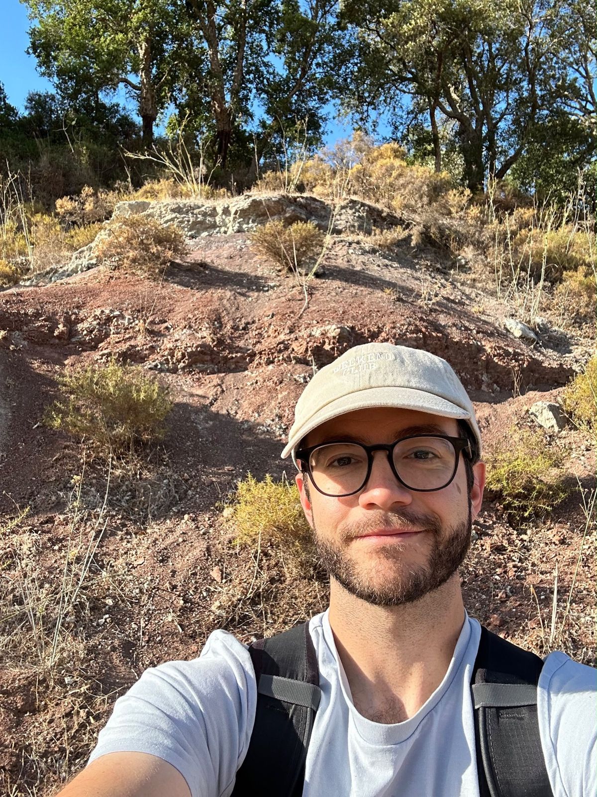 Miguel Marx in a cap and glasses in front of a red and grey rock outcrop under trees