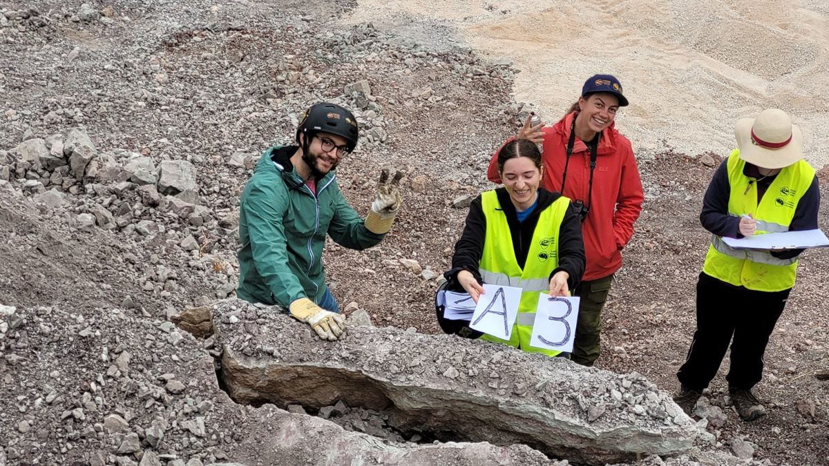 4 team members smiling around a long block of rock, one holding up paper signs reading A and 3