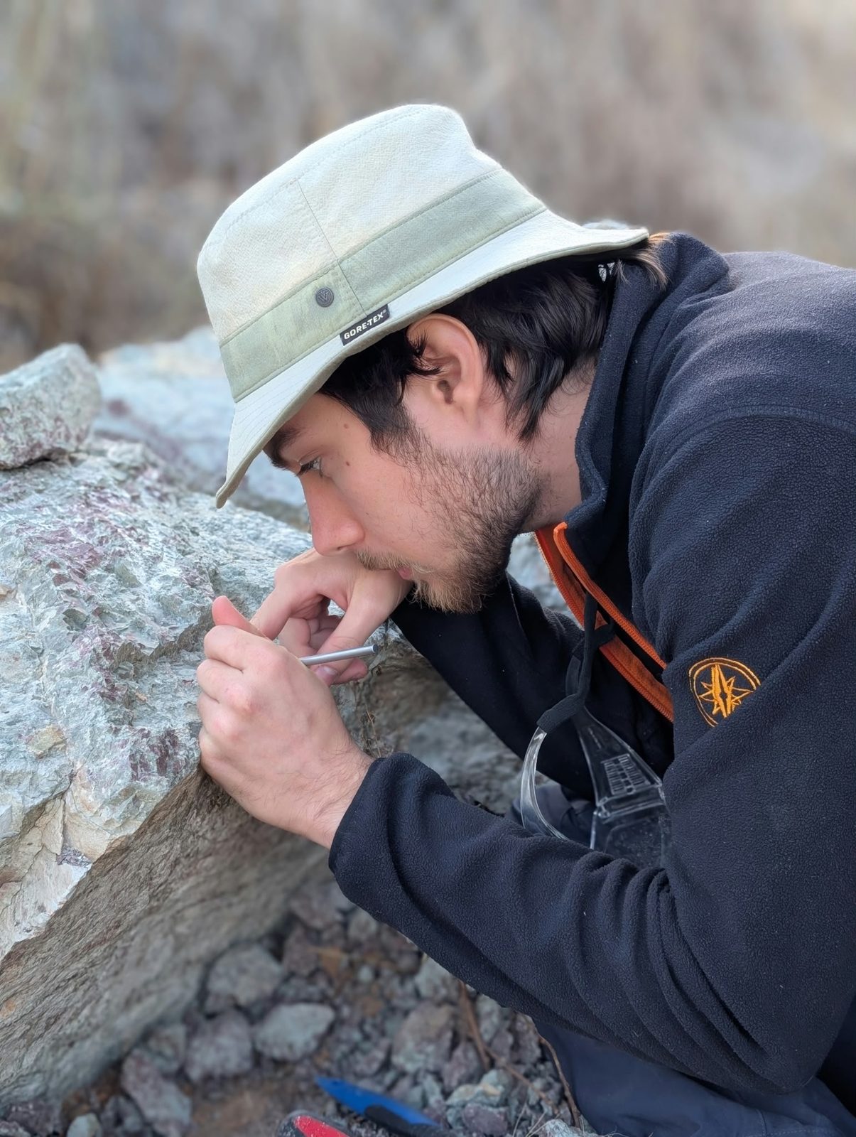 A team member in a bucket hat looking closely at a block of rock while working with a thin metal tool