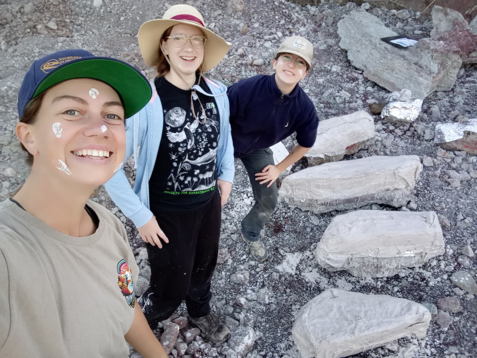 3 smiling team members with plaster on their faces, standing beside 4 white plaster jackets