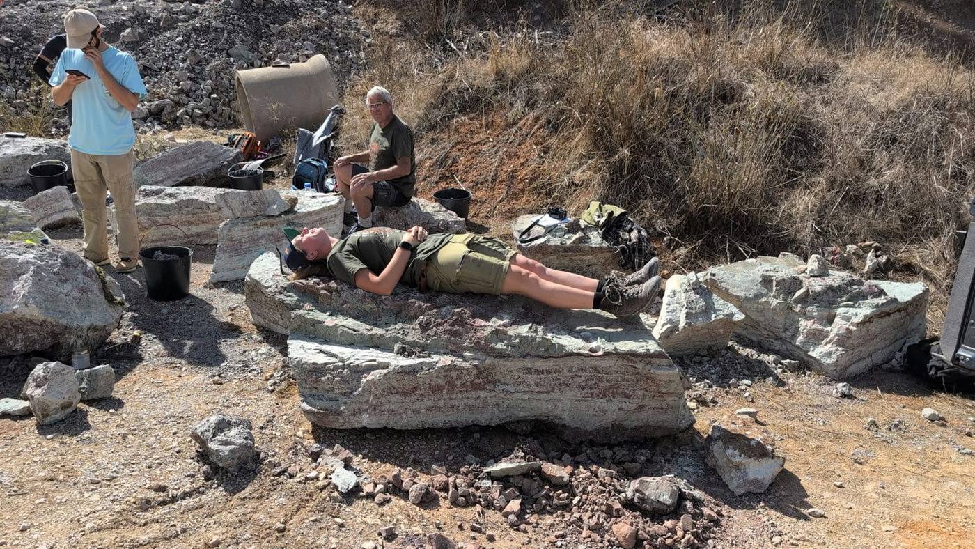 A team member lying flat on top of a large pale block of rock, with other blocks and team members around it