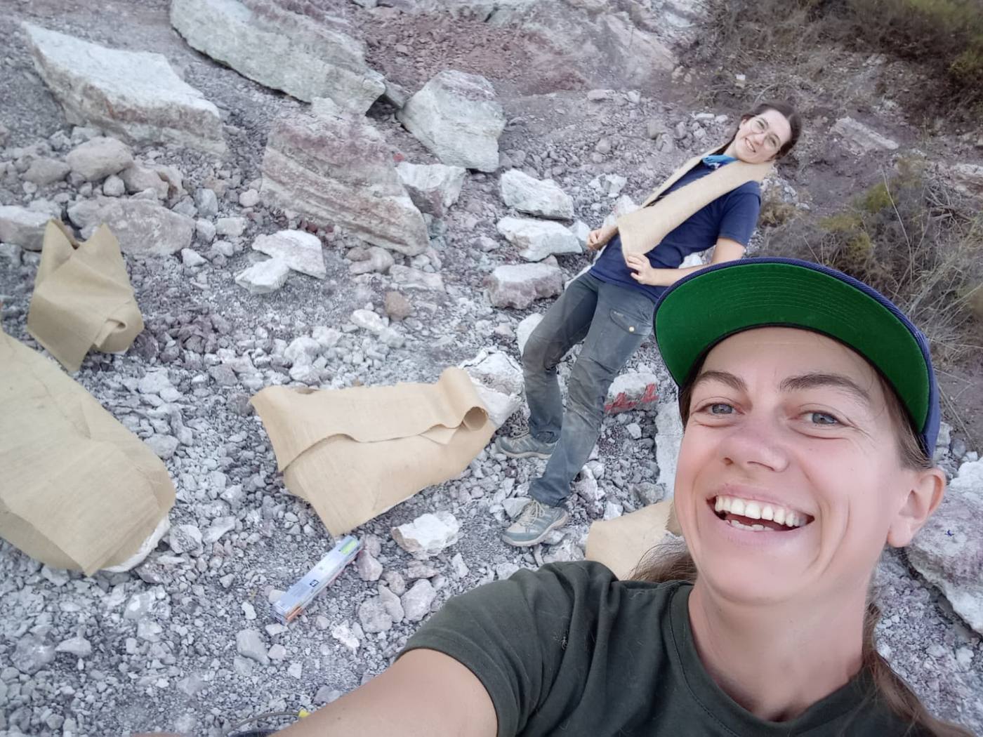 2 smiling team members among pale blocks of rock, some of them draped in strips of burlap