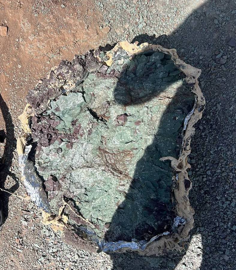 An opened plaster jacket lined with foil, holding a slab of gray green rock on the ground