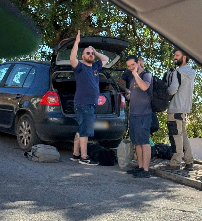 3 team members waving beside a car with its boot open and bags on the ground