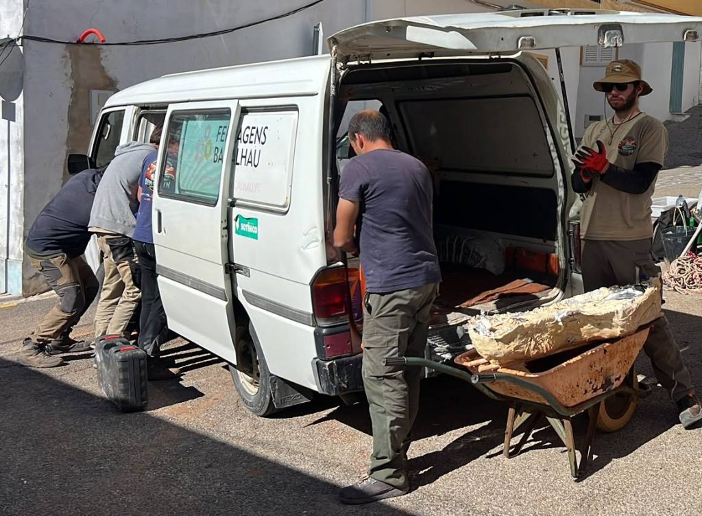 Team members loading a plaster jacket from a wheelbarrow into the back of a white van on a narrow street
