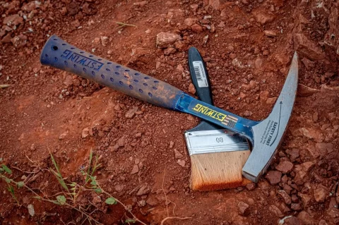Rock hammer and brush lying on red Algarve soil at the dig