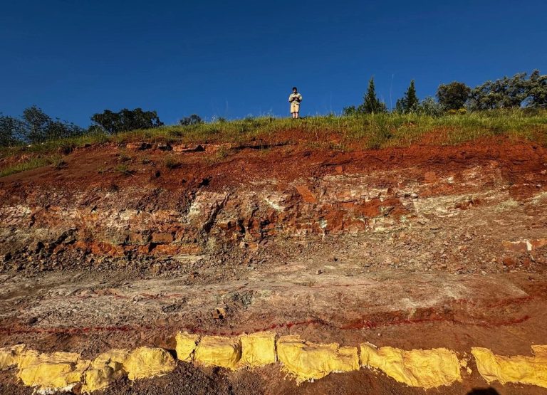 Layered red rock in a roadside cut, the base marked in yellow
