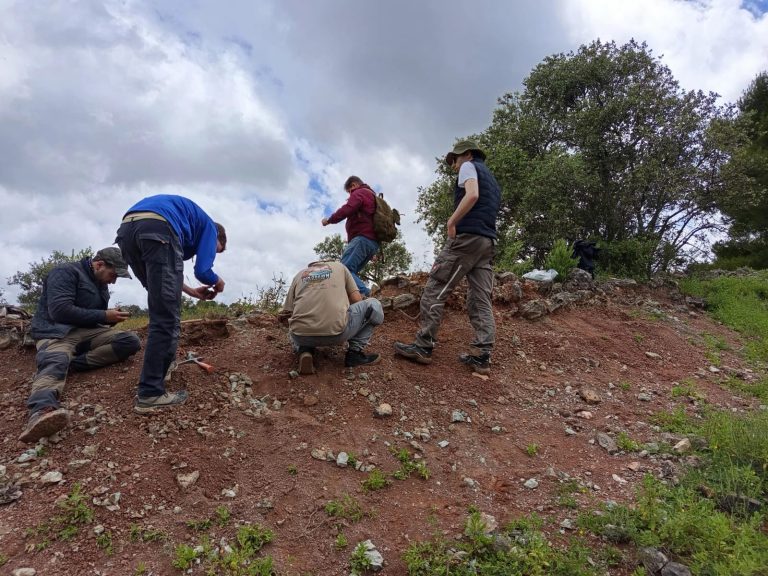 Team members searching the surface of a red hillside