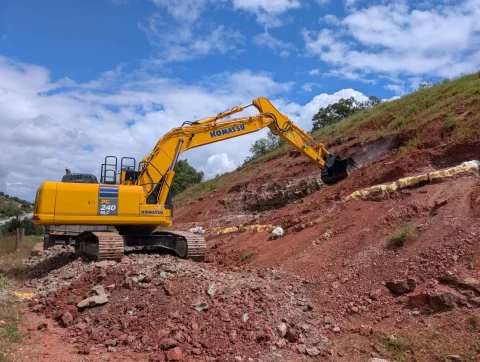 Excavator clearing a red slope beside plaster-jacketed blocks