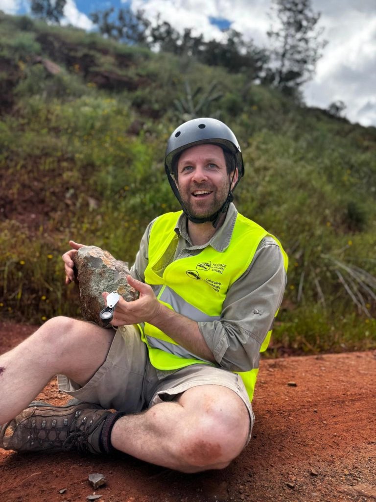 Team member in a helmet holding a rock and smiling