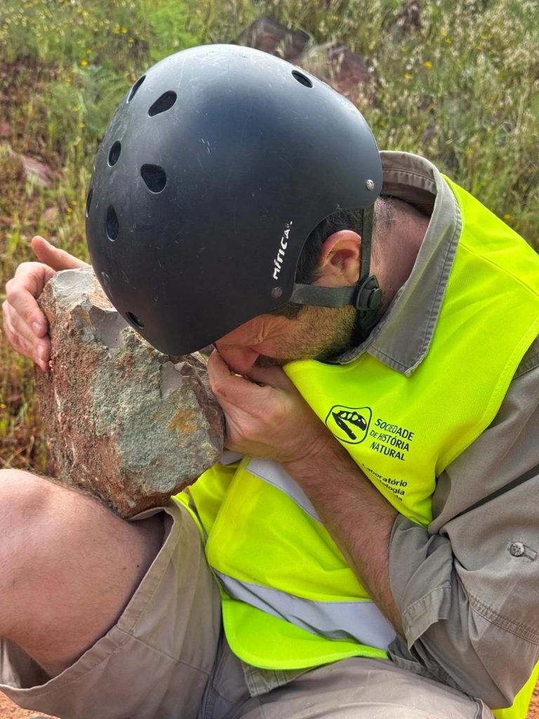 Team member in a helmet inspecting a rock with a hand lens