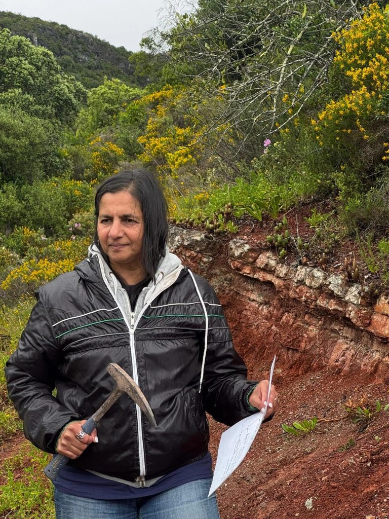 Team member with a rock hammer and field notes at an outcrop