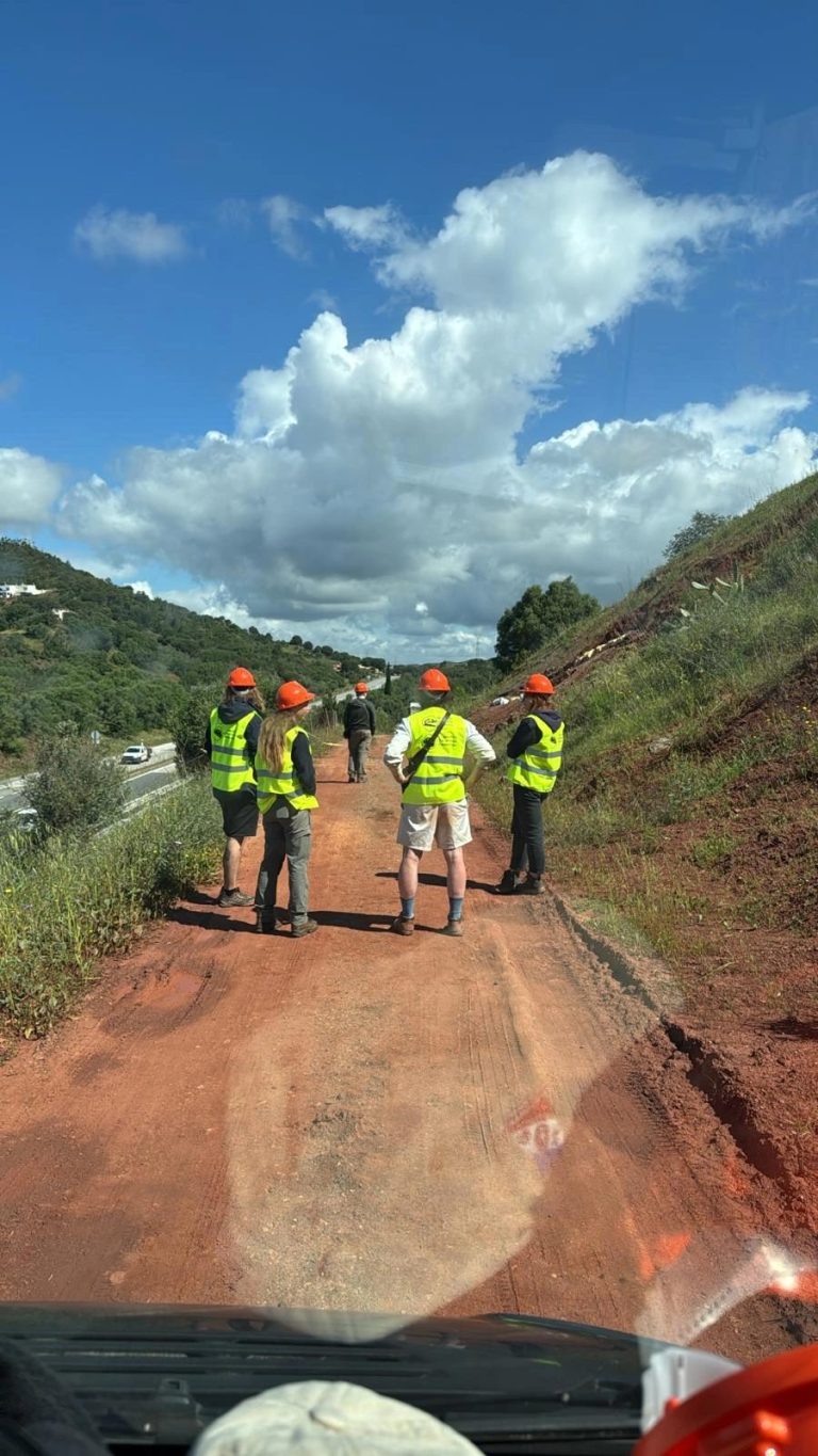 Team members in safety vests on a road between red slopes