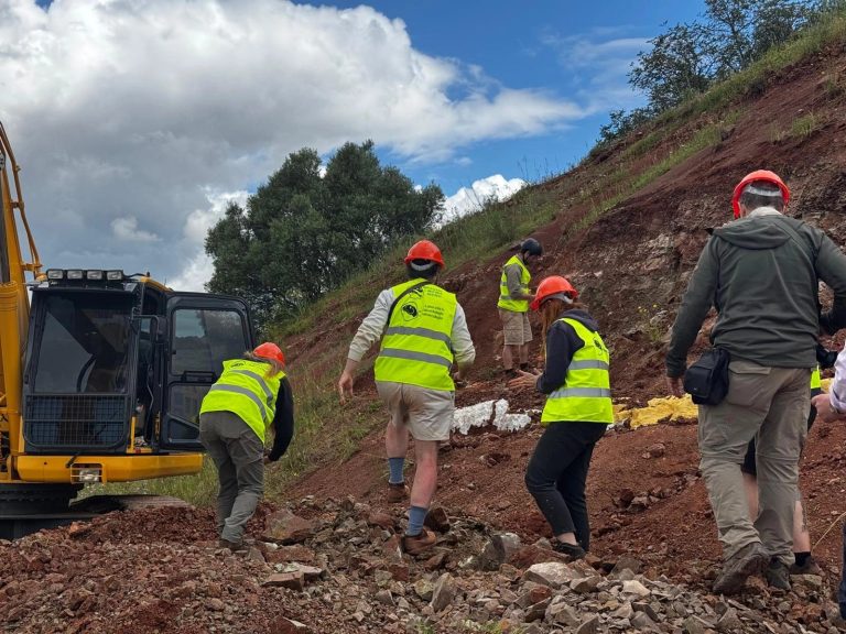 Field team climbing the slope beside the excavator