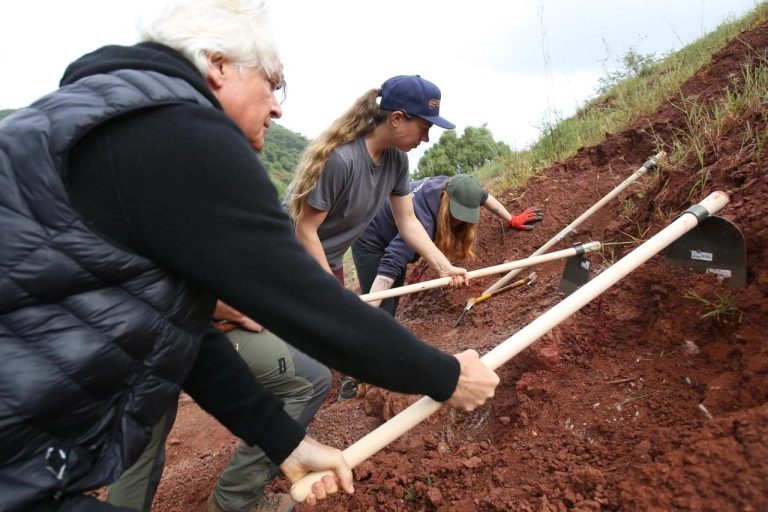 Team members scraping a red slope with long hoes