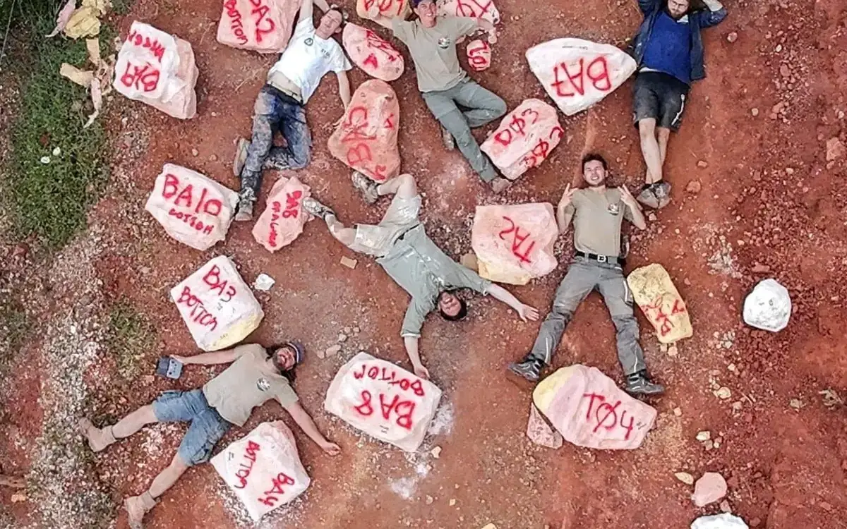 Plaster field jackets holding fossil blocks, laid out on red Algarve ground and seen from above, with team members lying among them.
